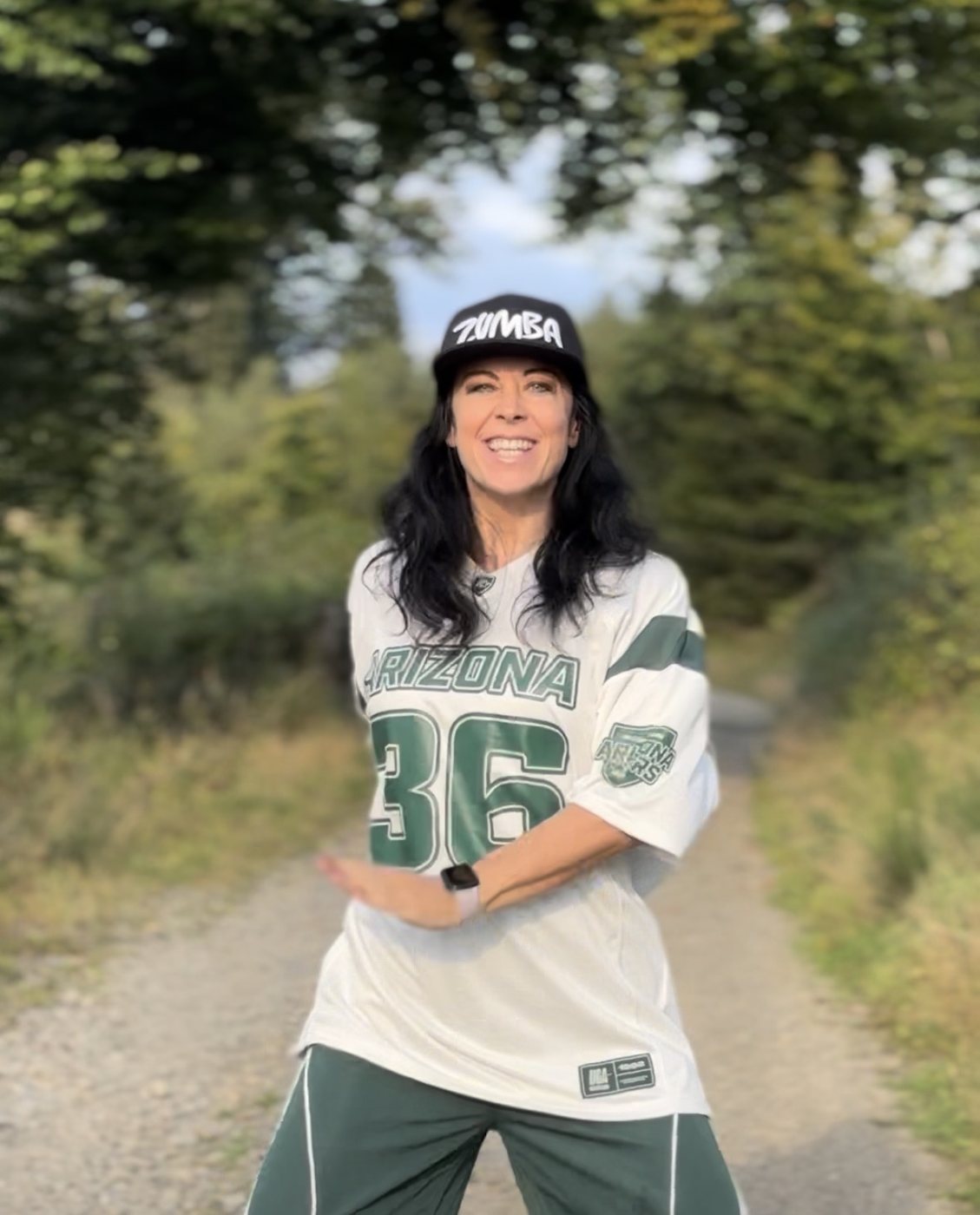 Elena tanzt lachend auf einem Waldweg, mit Zumba-Cap